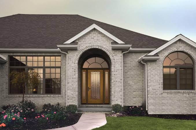 Contemporary luxury villa grand entrance with a bespoke pivot door, honed limestone masonry, and Mediterranean olive trees.